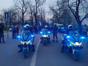 trzech policjantów na motocyklach stojących przed grupą oób biorących udział w przejeździe