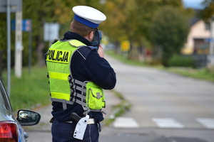 Policjant ruchu drogowego stoi przy drodze i mierzy prędkość pojazdów