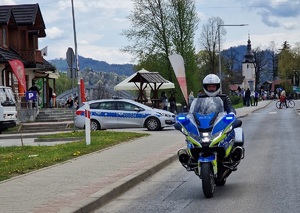 policjant na motocyklu a z prawe strony stoi zaparkowany radiowóz