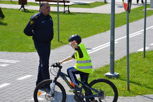 Chłopiec jadący na rowerze po miasteczku ruchu drogowego, obok nadzorujący jazdę gruziński policjant