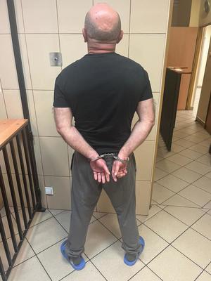zatrzymany stojący tyłem z kajdankami na ręce trzymane z tyłu w pomieszczeniu dla osób zatrzymanych przed osadzeniem
