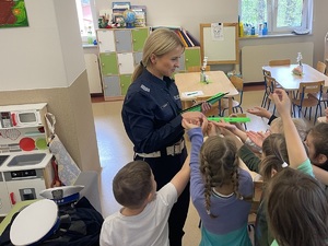 policjantka w sali przedszkola wręcza dzieciom opaski odblaskowe