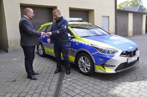KP Kęty burmistrz przekazuje kluczyli dzielnicowemu.  Za policjantem stoi nowy radiowóz marki Kia.
