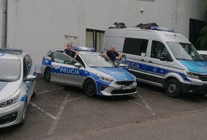 policjant i policjantka stojący przy radiowozie obok inne zaparkowane radiowozy