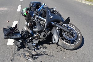 Motocykl po wypadku drogowym leżący na asfalcie,wokół niego oderwane części