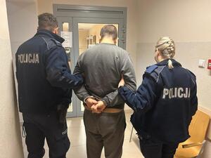 umundurowany policjanct i policjantka prowadzą zatrzymanego przez korytarz komisariatu