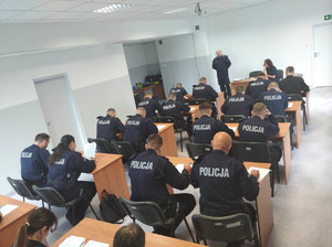 policjanci siedzą przy stolikach na sali i piszą test wiedzy
