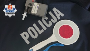 alcosensor wraz z tarcza do zatrzymywania samochodów na tle napisu policja wraz z logo KPP Sucha Beskidzka po lewej górnej stronie zdjęcia
