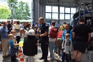 3 policjant pomaga założyć dziecku elemnty umundurowania, obok stoją inne dzieci i dorośli