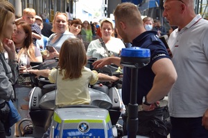 4 policjant stoi przy motocyklu, na którym siedzi dziewczynka, w tle ludzie