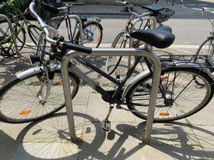 jeden z odzyskanych rowerów w kolorze czarnym oparty o stojak dla rowerów. W tle widać inne zaparkowane w pobliżu jednoślady