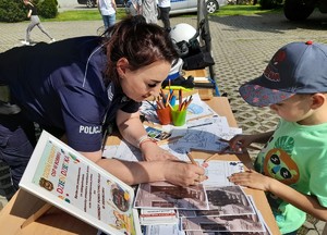 Piknik, stoisko policyjne, policjantka pomaga dziecku w kolorowaniu malowanki