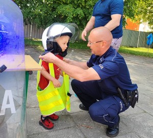 Piknik SP nr 5 w Oświęcimiu policjant przymierza dziecku elementy umundurowania  (1)