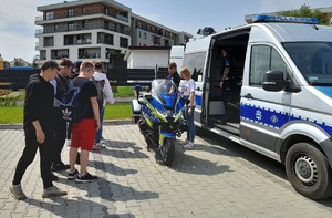 policjant prezentuje radiowóz i motocykl grupie młodzieży