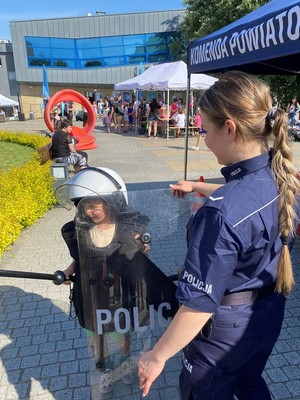 na zdjeciu unmundurowana funkcjonariuszka trzyma tarcze z naopisem Policja koło niej stoi dziecko ubrane w biały kask