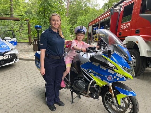Policjantka wraz z dziewczynką siedzącą na policyjnym motocyklu.