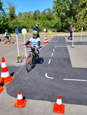 Chłopiec na rowerze jedzie po miasteczku ruchu drogowego, sędziują policjanci ruchu drogowego