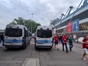 policyjne radiowozy ustawione tyłem do zdjęcia. Obok widać idących kibiców oraz stadion Wisły Kraków