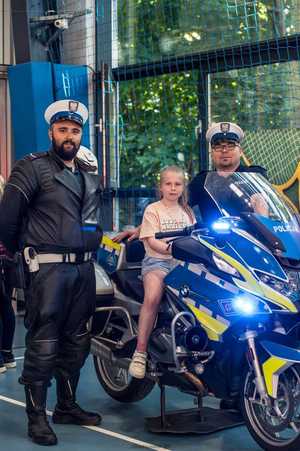 dwóch umundurowanych policjantów, pomiędzy nimi stoi motocykl policyjny, na którym siedzi młoda dziewczynka