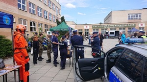 Funkcjonariusze stojący obok stoisk profilaktycznych i radiowozu na terenie liceum.