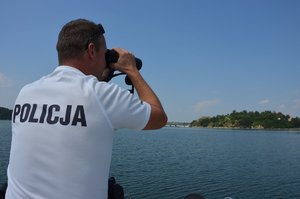 policjant patrolujący Jezioro Dobczyckie patrzący przez lornetkę