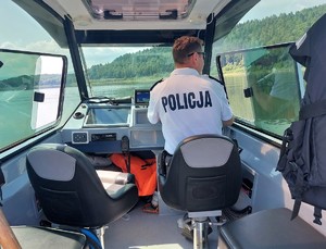 Na policyjnej łodzi motorowej siedzi na miejscu sternika umundurowany policjant.