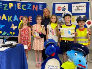 pamiątkowa fotografia uczniów w kamizelkach odblaskowych wraz z policjntką oraz maskotkami policyjnymi