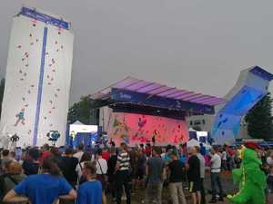 ścianki wspinaczkowe, na jedej z nich wspina sie mężczyzna zapięty w zabezpieczenie, dookoła stoją ludzie