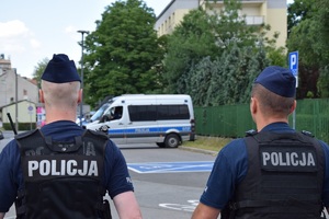 dwóch umundurowanych policjantów idących w kierunku ulicy Reymonta w Krakowie. W tle widać policyjny radiowóz