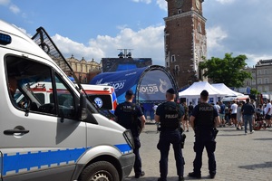 trzech umundurowanych policjantów stojących przy radiowozie obserwuje obiekt sportowy na krakowskim Rynku Głównym