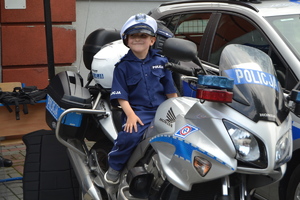 Chłopiec - uczestnik pikniku - przebrany za policjanta pozuje siedząc na motorze policyjnym