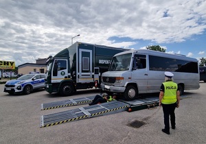 inspektor kontroluje zawieszenie busa policjantka stoi po prawej stronie
