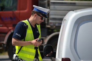Policjant trzymający w ręku urządzenie do badania trzeźwości, podczas rozmowy z kierującym zatrzymanym do kontroli