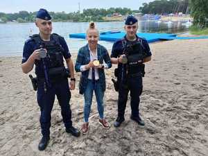 dwaj policjanci z zawodniczką trzymają w ręku medale, za nimi zalew