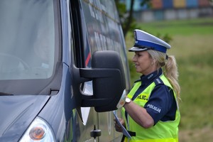 Policjantka ruchu drogowego wręcza kierującemu ulotkę z tabelą dopuszczalnych prędkości