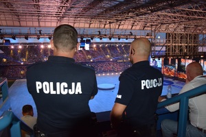 dwóch umundurowanych policjnaów stojących tyłem do zdjęcia obserwujących ceremonię zamknięcia igrzysk na obiekcie przy ul. Reymonta