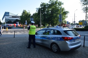 policjant ruchu drogowego stojący obok radiowozu, patrzy w kierunku osób w rejonie stadionu przy ul Reymonta