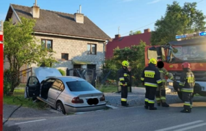 Srebrny samochód osobowy oraz strażacy i wóz strażacki