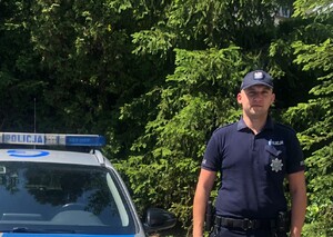 umundurowany policjant stojący przy radiowozie w tle drzwa