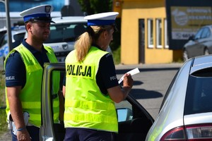 Policjant i policjantka ruchu drogowego wręczają ulotkę dotyczącą wyprzedzania kierującemu pojazdem