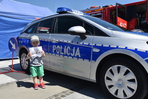 Dziecko z kolorowanką stojące obok policyjnego radiowozu