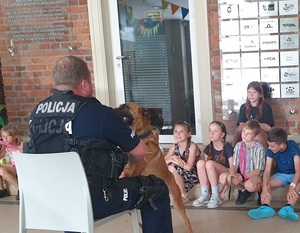 policyjny przewodnik psa opowiada grupie dzieci o swojej pracy