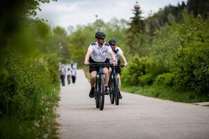 Dwóch policjantów na rowerach patroluje ścieżkę rowerową. W tle idące ścieżką osoby