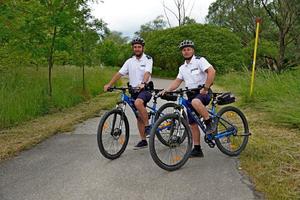 Dwóch policjantów z rowerami stoi na ścieżce rowerowej.