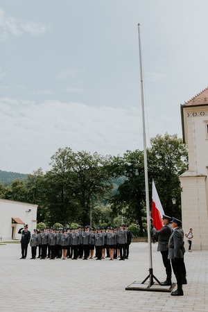 sztadar wciagany na maszt na tle policjantów śpiewający głosno Hymn Polski