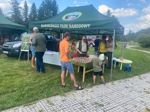 Stoisko babiogórskiego Parku Narodowego oraz osoby w tym dziecko z watą cukrową biorace udział w konkursie wiedzy