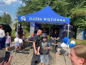 Stoisko Słuzby więziennej odwiedzane przez ososby i chłopczyk przebrany w strażnika trzymający tarczę