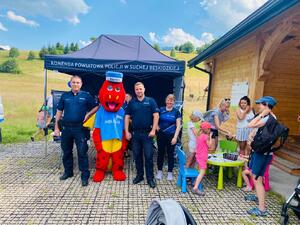 Stoisko Suskiej Policji i pozujący policjanci i pracownica Policji a obok stolik przy ktrym dzieci rozwiązują krzyżówki