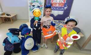 przedszkolaki na pamiątkowym zdjęciu z maskotkami policyjnymi prezentują elemnty umundurowania