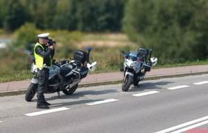 policjant mierzy prędkość obok niego na poboczu dwa zaparkowane motocykle